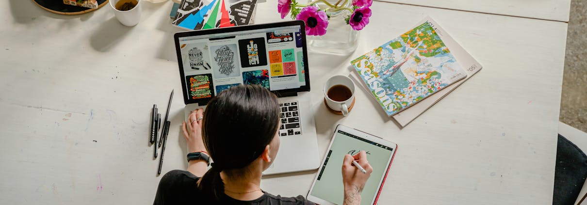 Photo of Woman Writing on Tablet Computer While Using Laptop